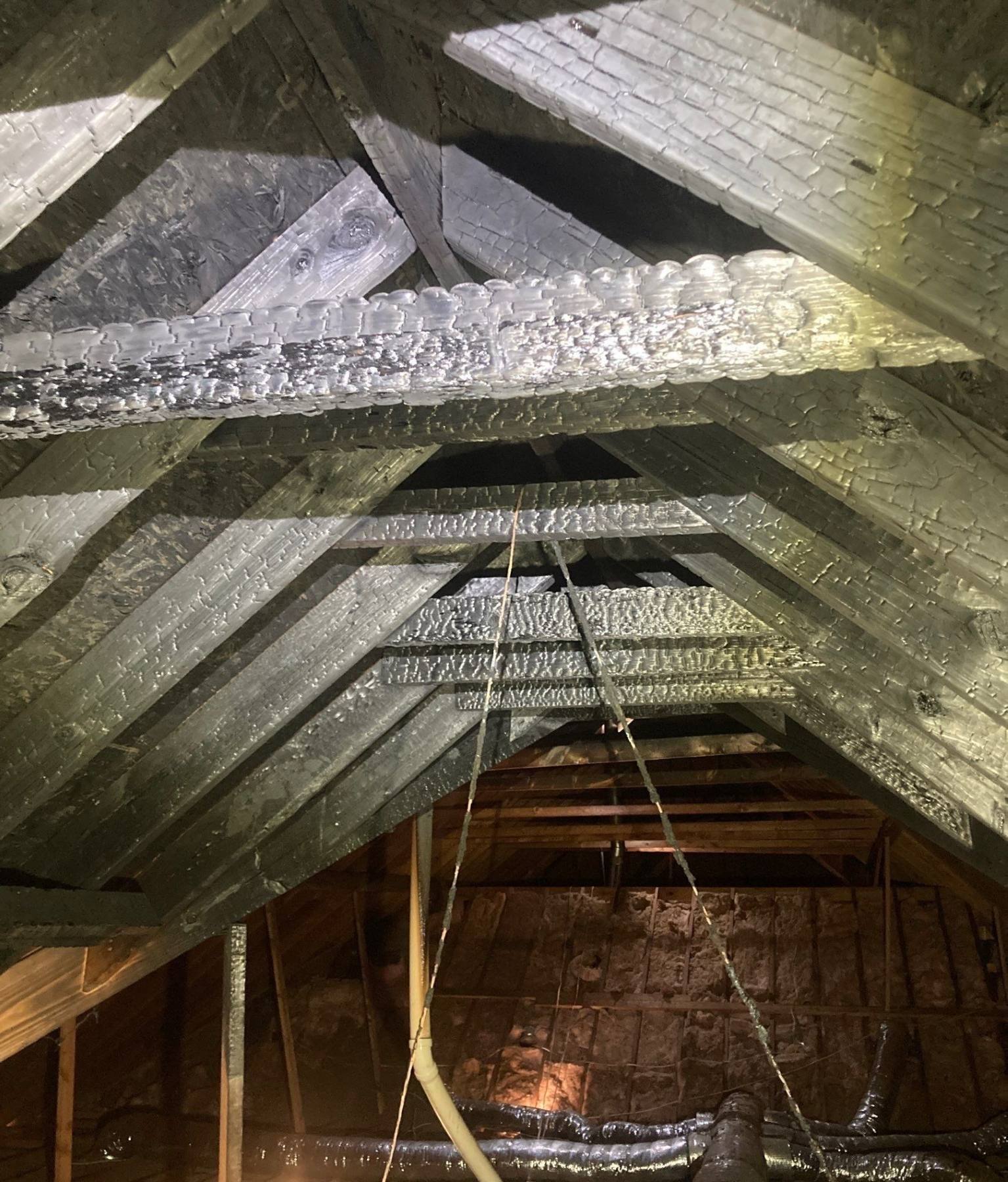 Close view of heavily charred roof rafters and structural framing after fire damage