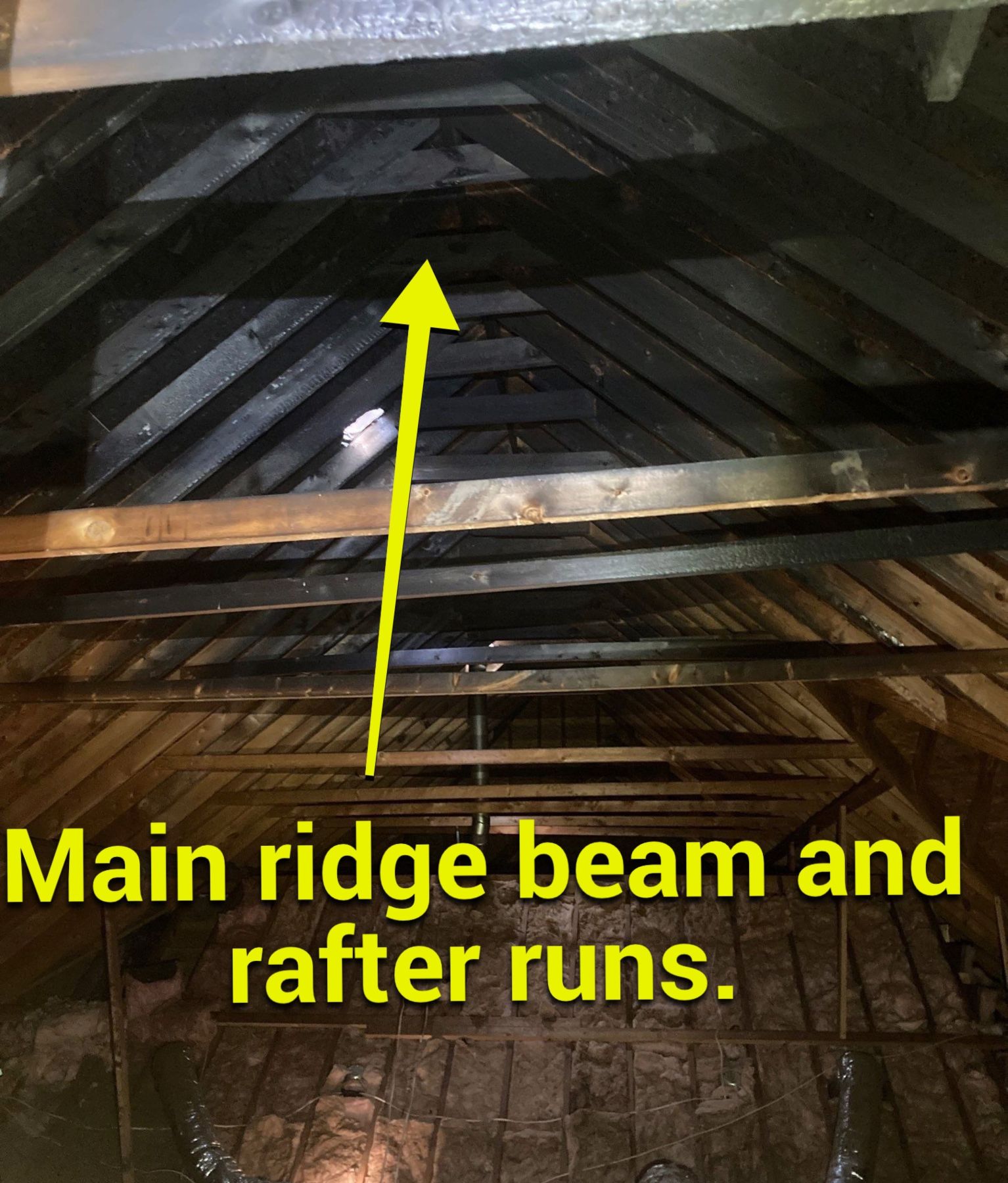 Fire-damaged roof framing with charred rafters and main ridge framing visible during attic inspection