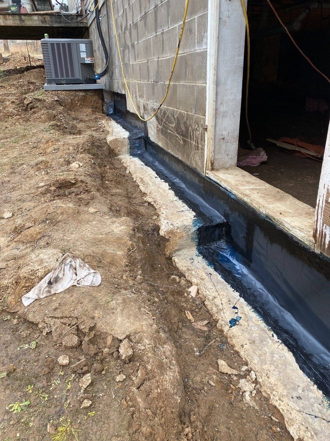 Foundation waterproofing and French drain work along an excavated concrete masonry foundation wall