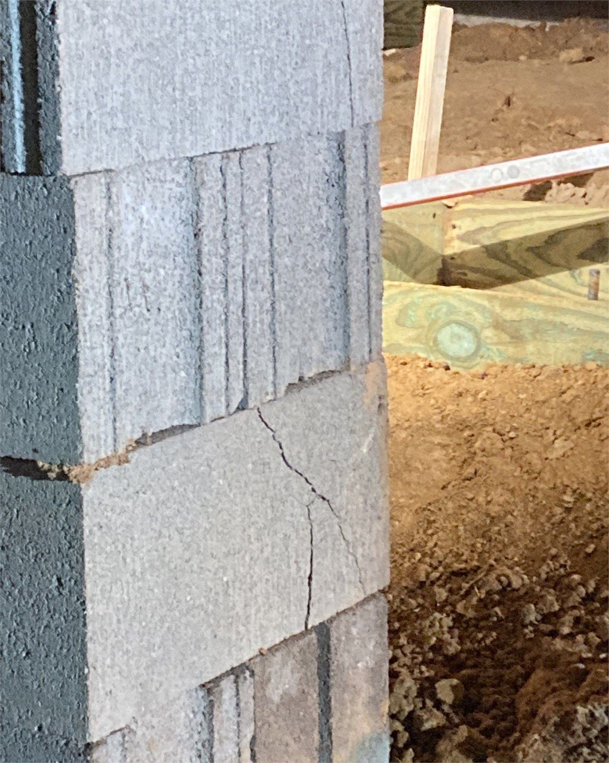 Crack damage visible in a pier foundation support inside a crawlspace