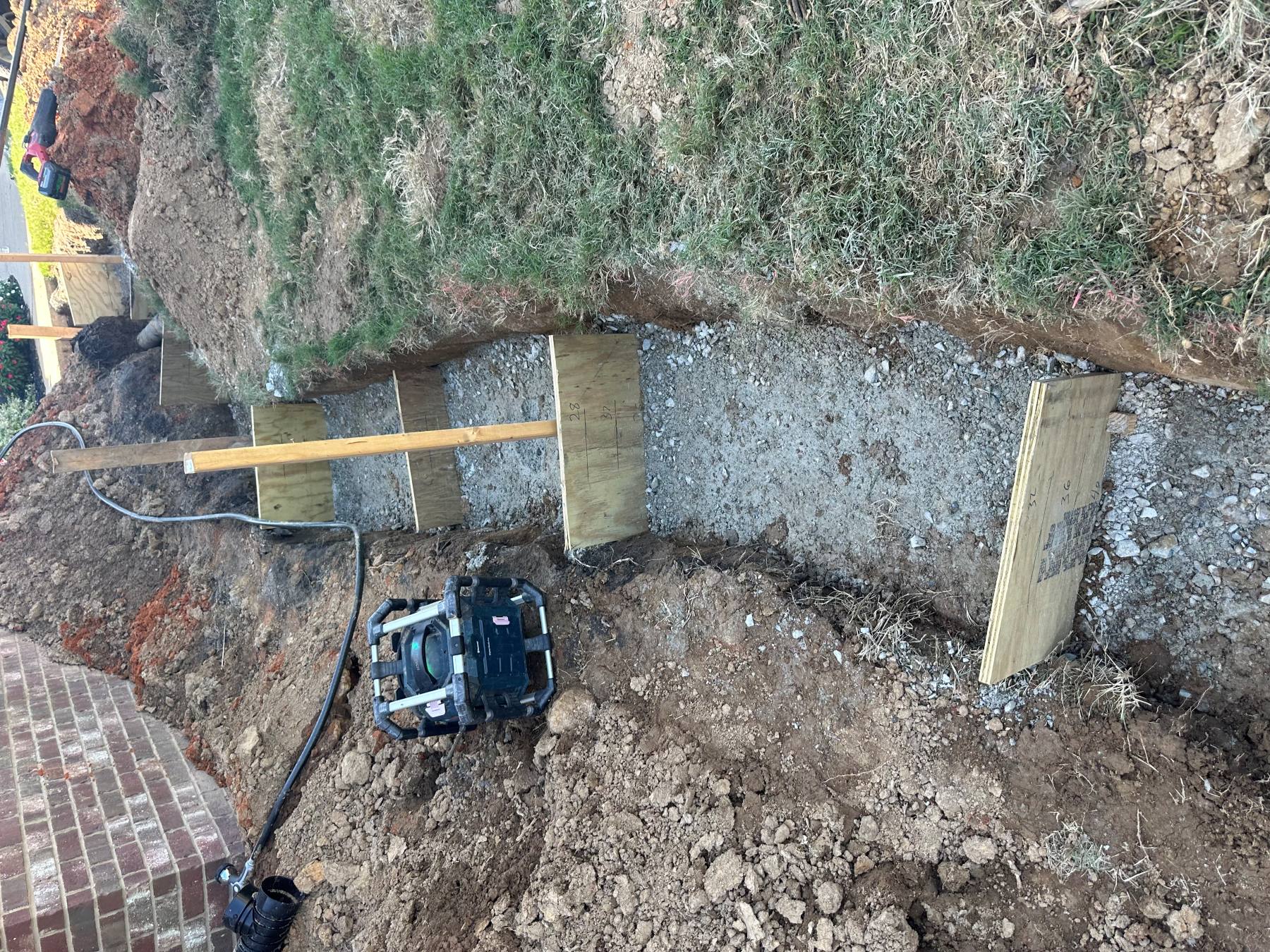 Aggregate retaining wall base with compaction equipment inside the excavated trench