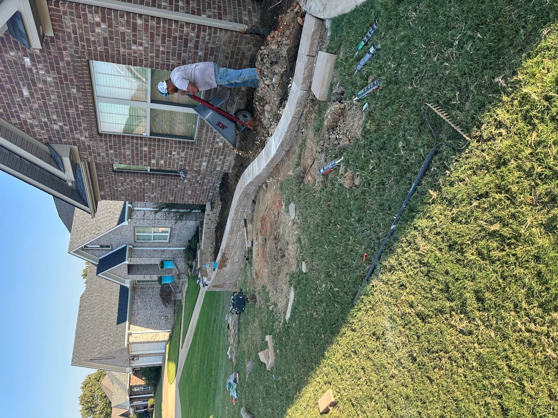 Wide excavation following the planned curved retaining wall route beside a building