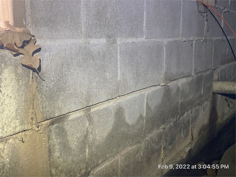 Horizontal crack visible across a concrete masonry foundation wall in a crawlspace