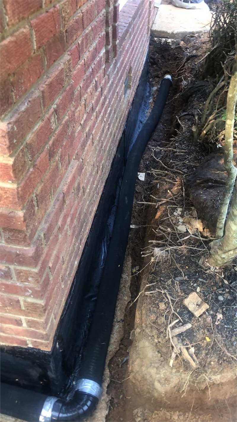 Drainage and waterproofing correction installed beside a brick foundation wall