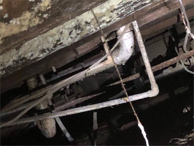Open floor cavity exposing deteriorated wood framing, plumbing, insulation, and concealed mold-related property damage.